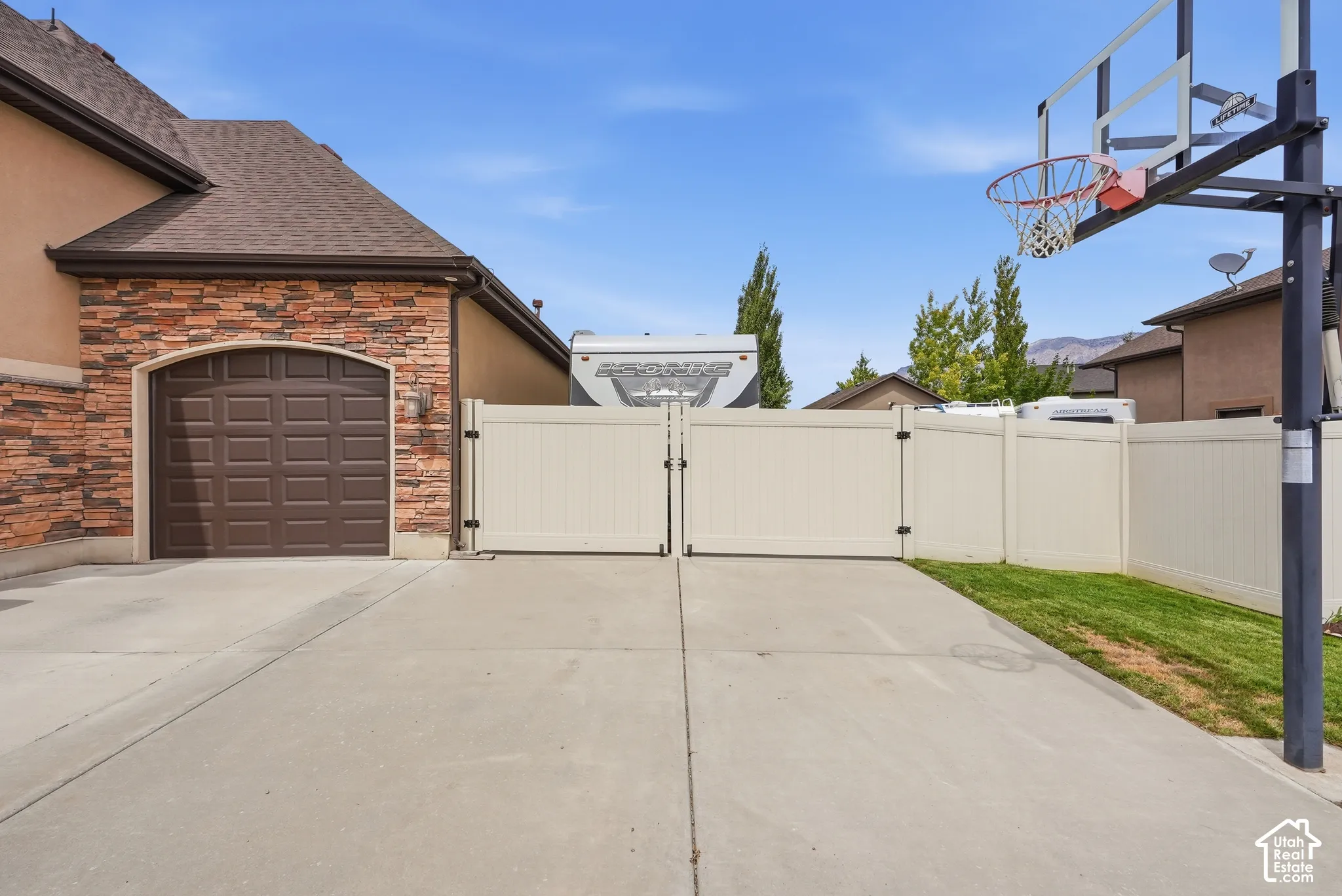 Expansive concrete driveway with a basketball hoop, leading to a garage with a paneled door
