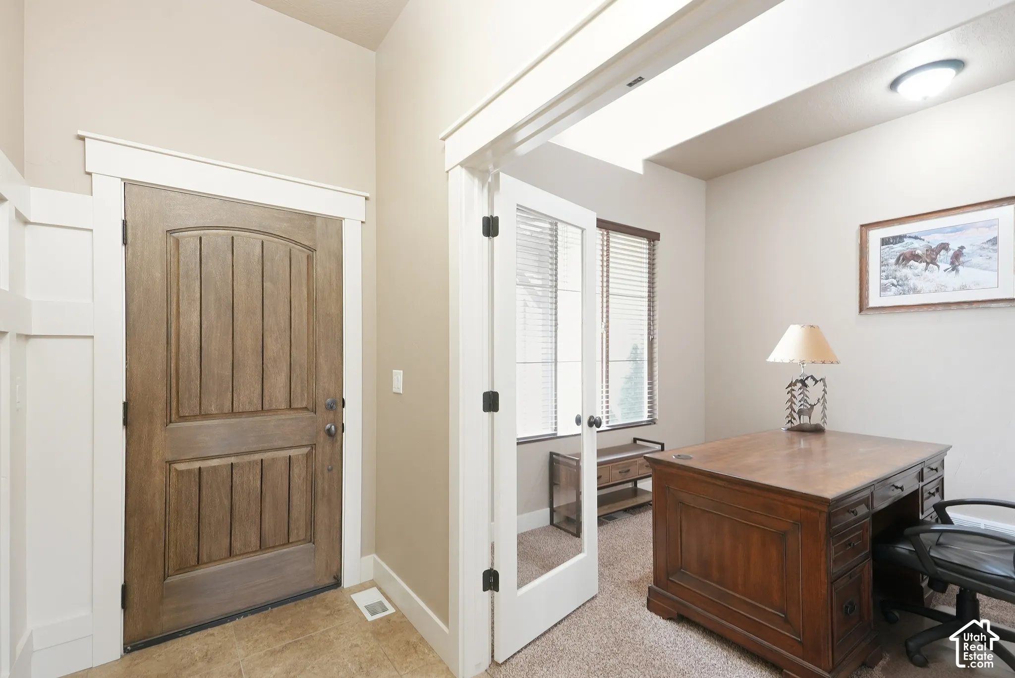 Arched wood-panel entry door, white trim, tiled flooring, French doors, and a window with blinds