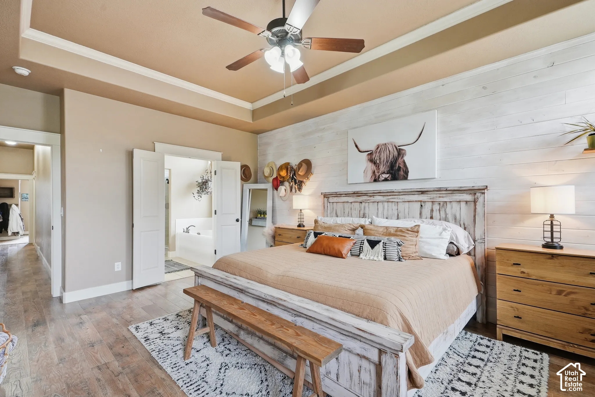 Wood-finish flooring, recessed ceiling with crown molding, double doors, and a decorative accent wall