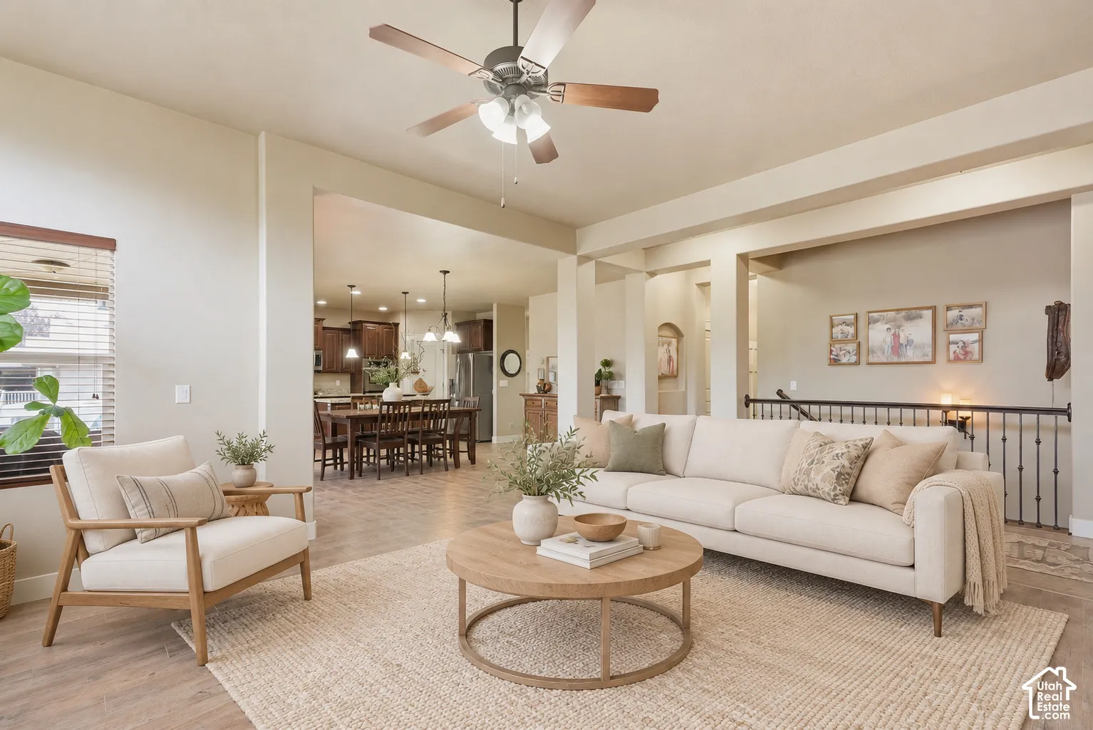 Open-concept main living area featuring wood-finish flooring, recessed lighting, a ceiling fan with integrated light fixture, and wrought iron stair railing