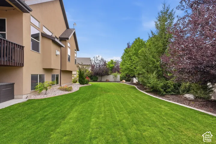 Expansive lawn area with a defined landscape border, mature trees, and a multi-level exterior with a wooden balcony