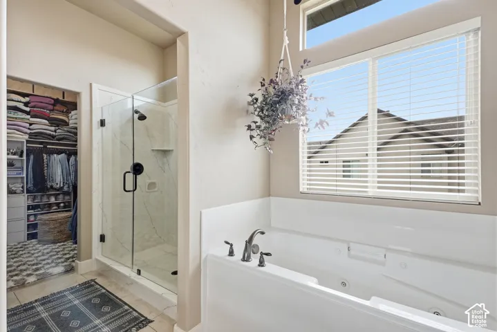 Built-in soaking tub with dark-finish fixtures, clear glass shower enclosure with dark-finish hardware, organized walk-in closet, and an upper transom window
