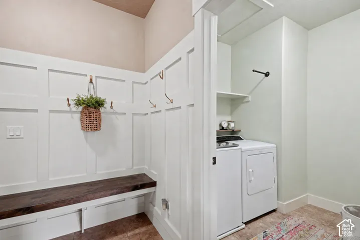 Mudroom featuring wainscoting, a built-in wooden bench, integrated coat hooks, and an adjacent laundry area with built-in shelving