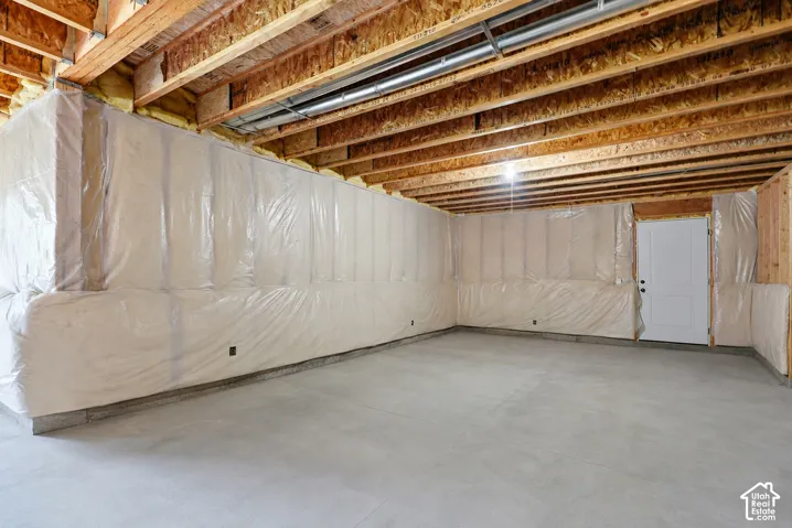 Unfinished basement with exposed wood joists, concrete flooring, and insulated perimeter walls