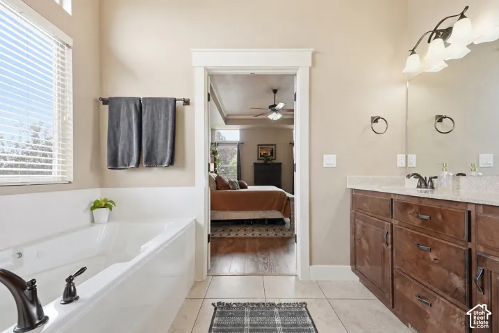 Spacious bathroom featuring a built-in soaking tub, a window with blinds, and a vanity with a light-toned countertop