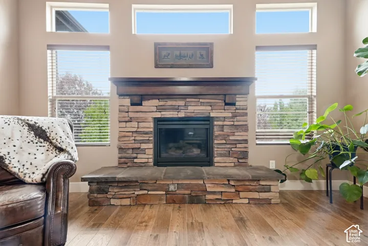 Stacked stone fireplace with a dark wood mantel, integrated firebox, wood-finish flooring, and multiple windows