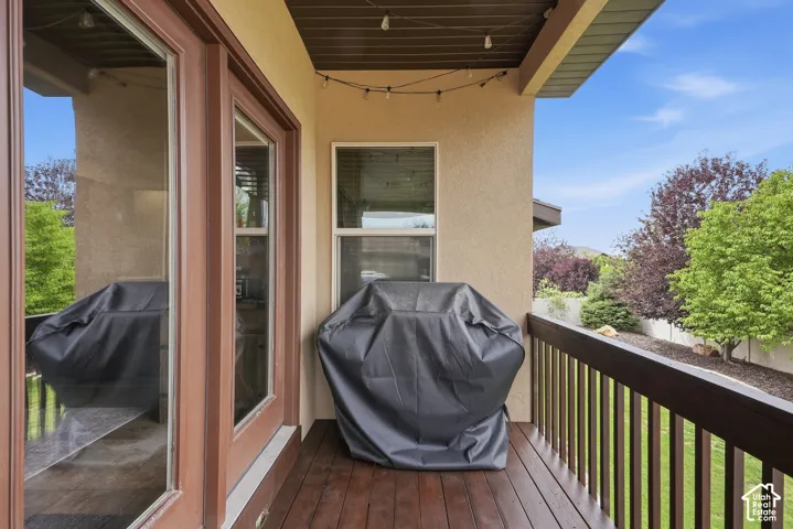 Outdoor deck with wood-finish flooring, featuring a dark wood railing, stucco exterior, and overhead lighting