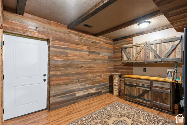 Interior space featuring wood-plank wall paneling, exposed ceiling beams, built-in wooden cabinetry with X-brace detailing, and a countertop workspace