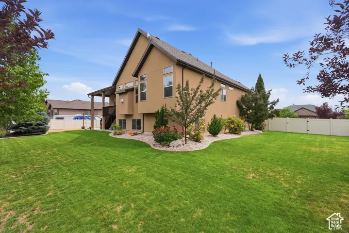 Expansive backyard featuring a manicured lawn, established landscaping, and a tan vinyl fence