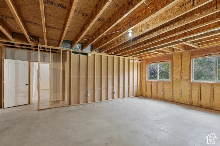 Unfinished lower level with exposed ceiling joists, concrete flooring, and multiple windows