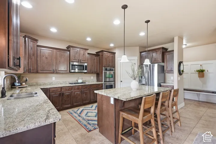 Kitchen featuring granite countertops, dark wood-finish cabinetry, stainless steel appliances, and an island with pendant lighting