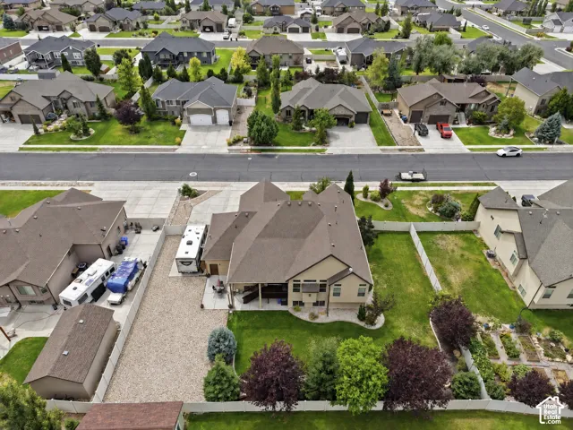 Aerial perspective of a multi-level residence featuring a shingled roof, an expansive side-yard gravel area, a private lawn, and an attached covered porch