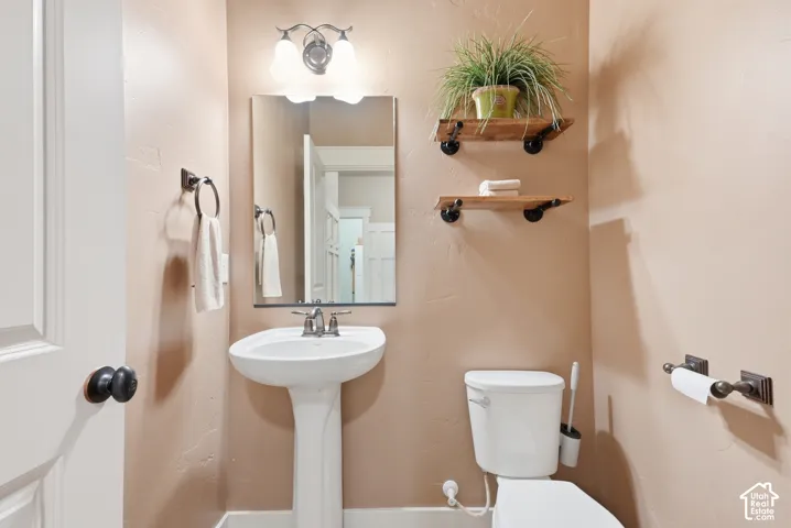 Pedestal sink with a coordinating wall-mounted mirror, two-light vanity fixture, and industrial-style shelving