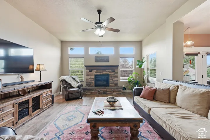 Vaulted ceiling with a ceiling fan, stone-surround fireplace with a wood mantle, multiple windows providing natural light, and wood-finish flooring