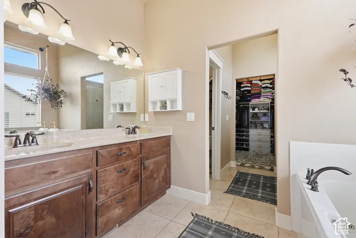 Double vanity with wood-finish cabinetry and bronze fixtures, integrated soaking tub, tiled flooring, and a walk-in closet with built-in shelving