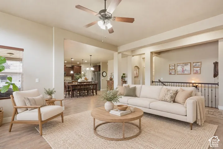 Open-concept main living area featuring wood-finish flooring, recessed lighting, a ceiling fan with integrated light fixture, and wrought iron stair railing