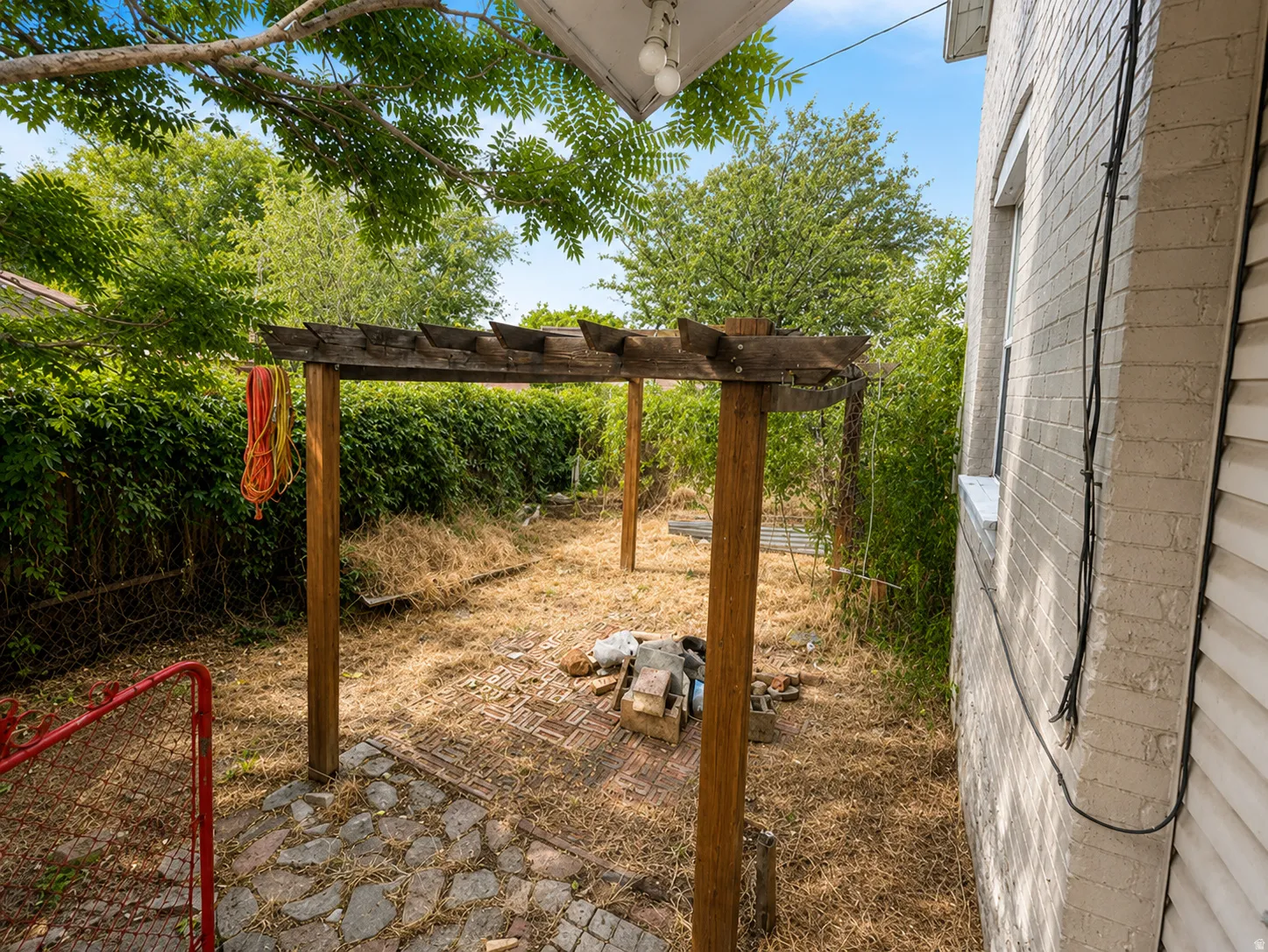 Wood pergola structure, stone paver patio, painted brick exterior, and lush perimeter greenery