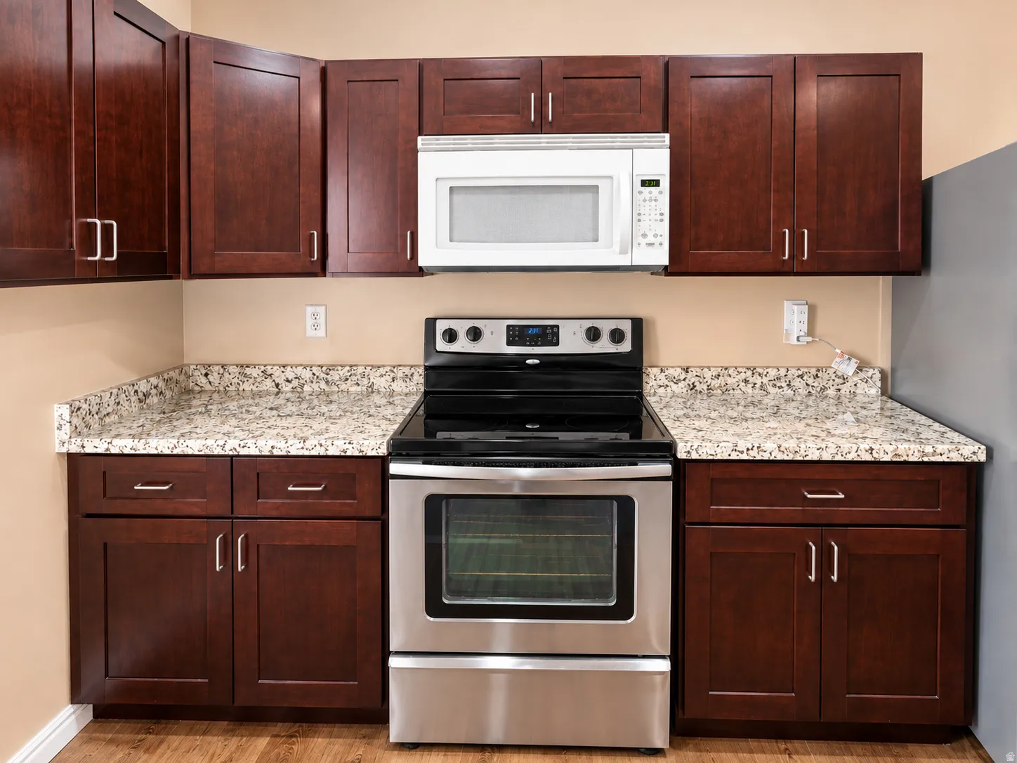 Dark wood-finish cabinetry, light speckled countertops, stainless steel range, and an over-the-range microwave