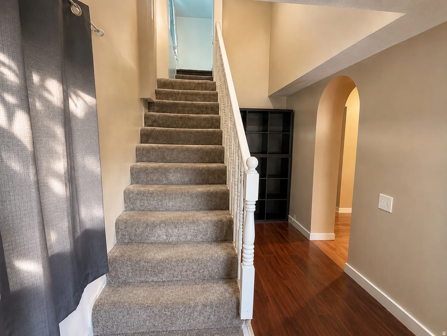 Carpeted staircase with white balusters, wood-finish flooring, and an arched doorway