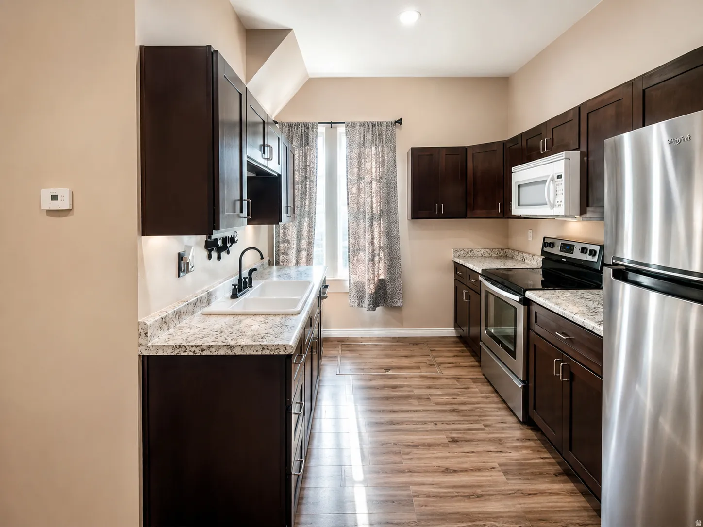 Kitchen featuring dark wood-finish cabinetry, light-toned countertops, wood-finish flooring, a stainless steel refrigerator, and a built-in microwave