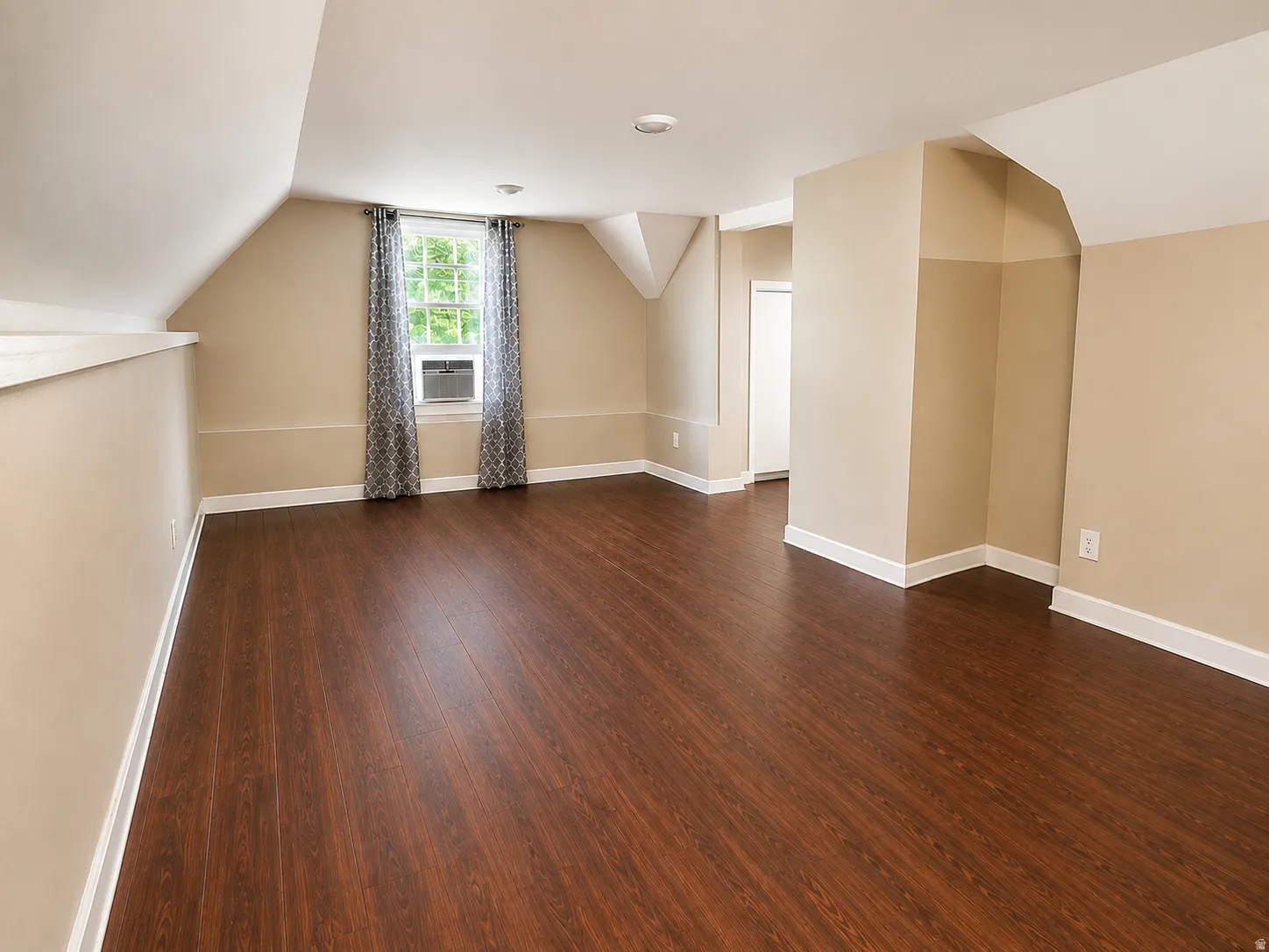 Spacious room featuring wood-finish flooring, neutral paint, a window with natural light, and sloped ceilings