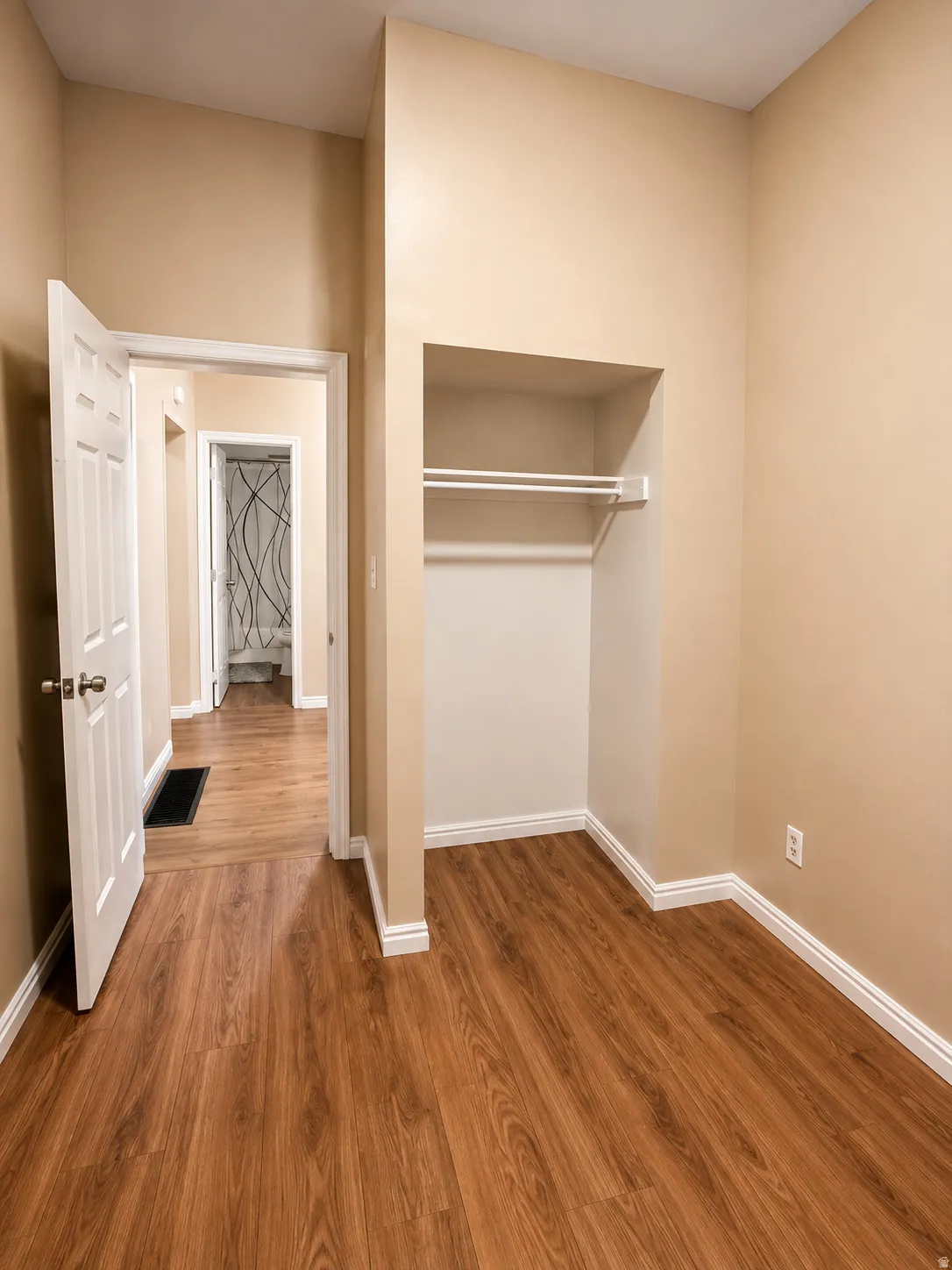 Wood-finish flooring throughout, light neutral wall paint, and a built-in closet with hanging rod