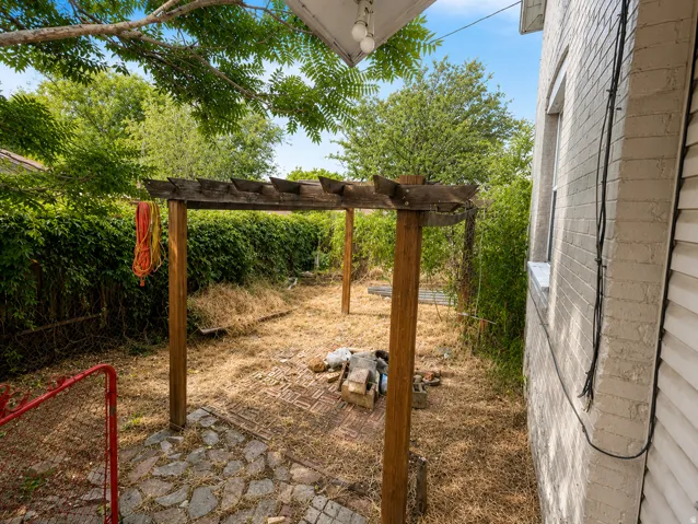 Wood pergola structure, stone paver patio, painted brick exterior, and lush perimeter greenery