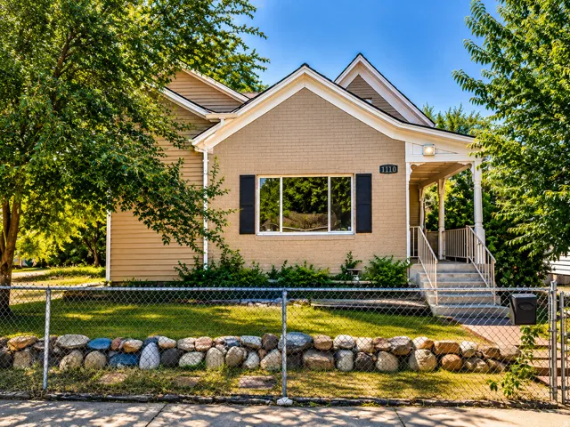 Exterior featuring brick and siding finishes, a covered front porch with decorative columns, a chain-link fence, and a stone retaining wall