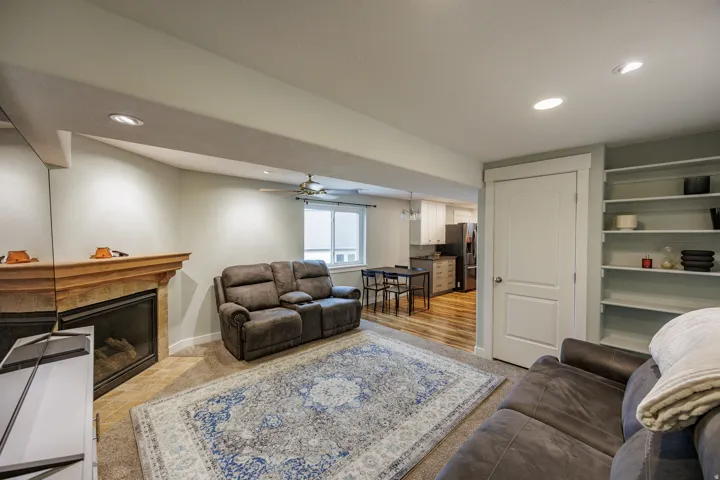 Recessed lighting, a built-in fireplace with a stone surround and wood mantel, built-in shelving, a ceiling fan, and wood-finish flooring