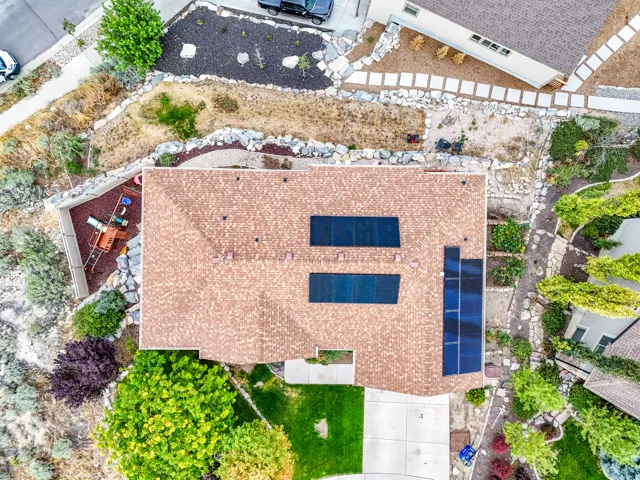 Shingle roof with installed solar panels, concrete driveway, and established landscaping