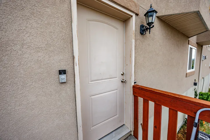 Stucco exterior with a paneled entry door, exterior sconce lighting, and wood railing