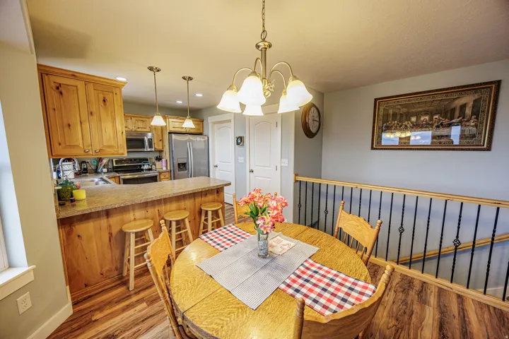 Open-concept dining space featuring wood-finish flooring, a contemporary chandelier, and a wood railing with black metal spindles