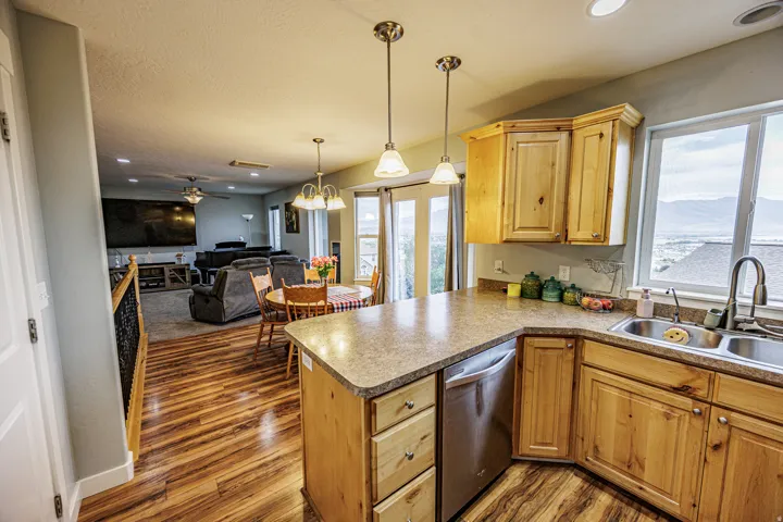 Kitchen featuring wood-finish flooring, light wood cabinetry, a double basin sink, and an integrated dishwasher