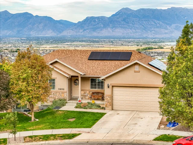 Stucco exterior with stone accents, attached two-car garage, solar panels, and a concrete driveway
