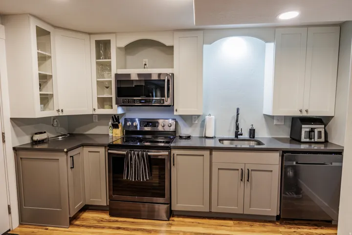 Kitchen featuring wood-finish flooring, two-tone cabinetry, stainless steel appliances, a built-in microwave, and a stainless steel sink with a matte black faucet