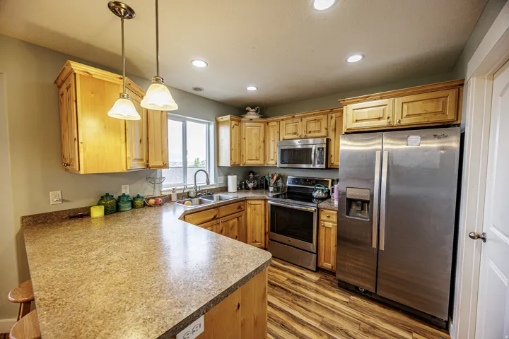 Kitchen featuring wood cabinetry, stainless steel appliances, a corner sink, recessed lighting, and wood-finish flooring