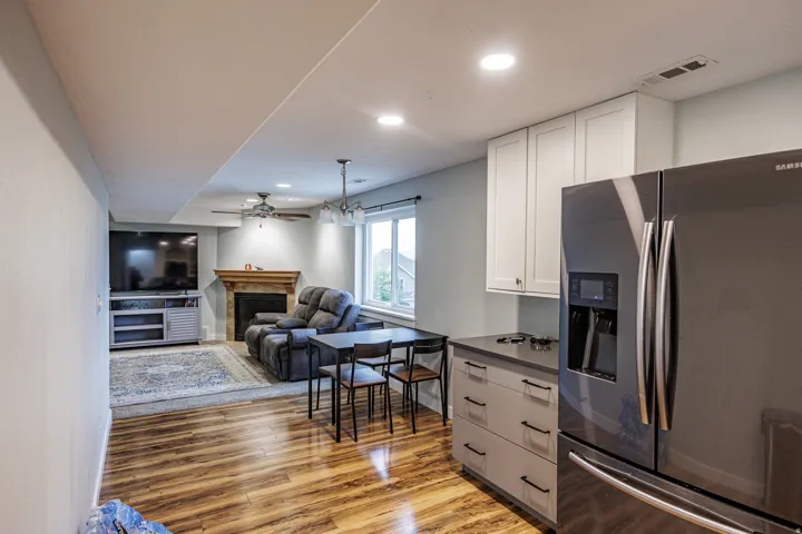 Wood-finish flooring, built-in cabinetry with a countertop, stainless steel refrigerator, recessed lighting, and a fireplace with a mantel