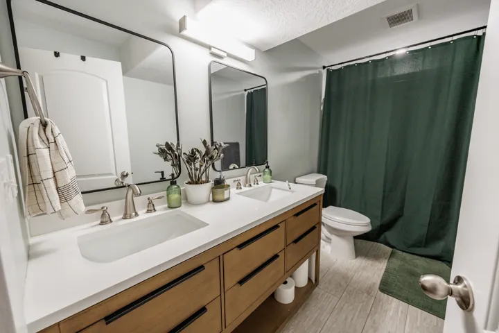 Dual vanity with integrated sinks, brushed nickel fixtures, wood-finish cabinetry, and framed mirrors