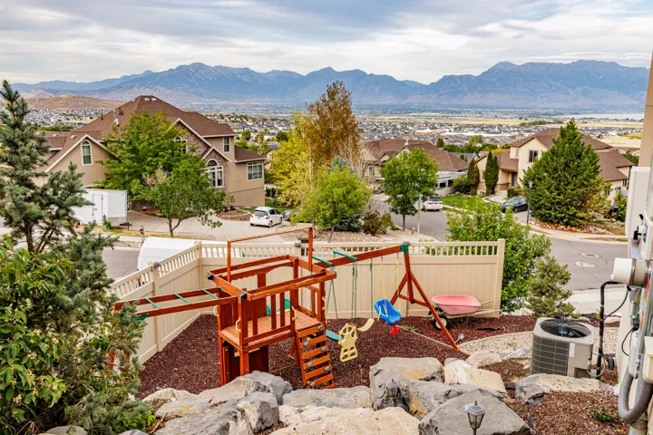 Terraced backyard with a playset, wood chip ground cover, and a light-toned privacy fence