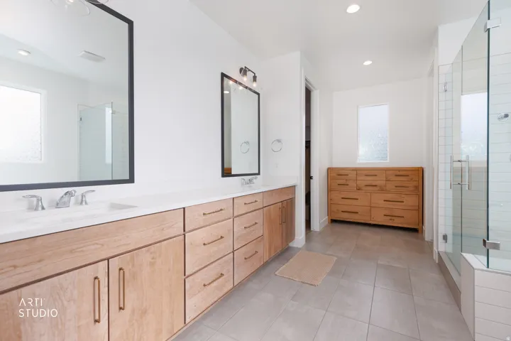 Dual vanity with light wood-finish cabinetry, white countertops, and chrome fixtures