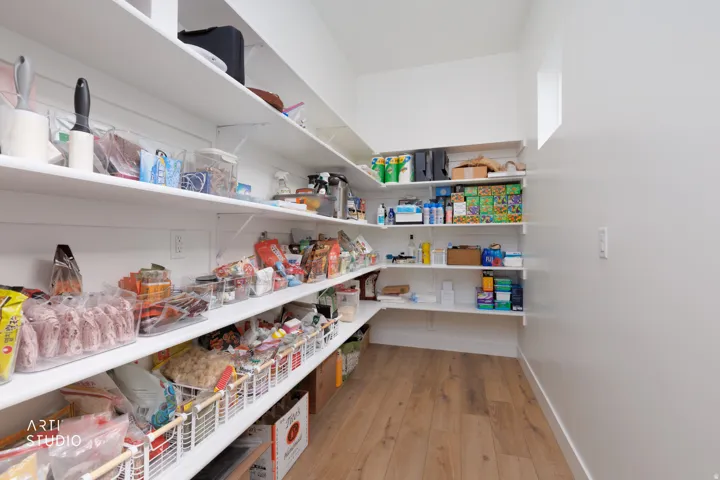 Walk-in pantry featuring extensive white shelving, wood-finish flooring, and a high ceiling