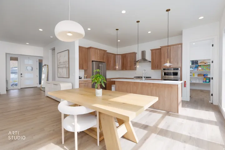 Expansive wood-finish flooring throughout, kitchen featuring light wood cabinetry, a large kitchen island with white countertop, stainless steel appliances, and a dedicated pantry
