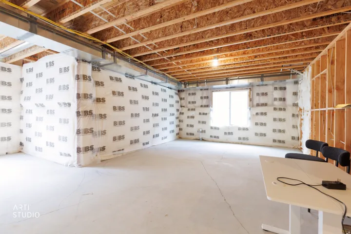 Unfinished interior space with exposed ceiling joists and wall studs, featuring a concrete floor and a single window