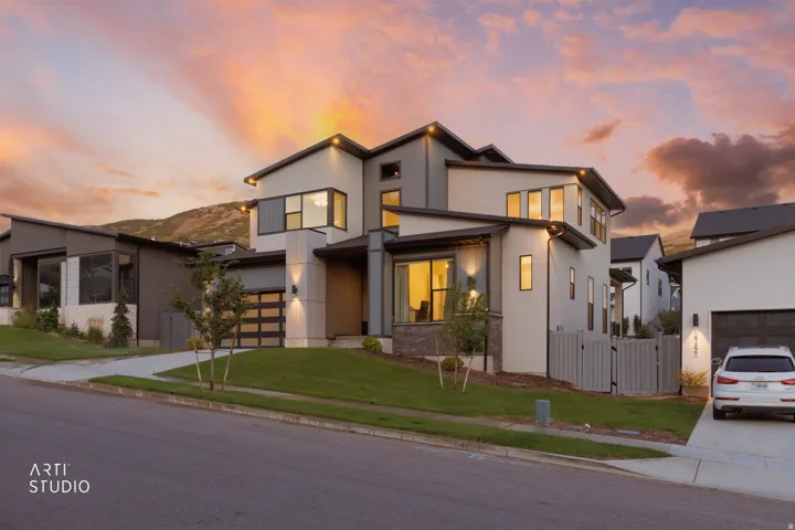 Modern architectural style, multi-level dwelling, integrated garage with glass-paneled door, exterior accent lighting, and a manicured lawn