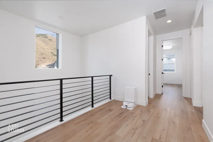 Wide plank wood-finish flooring, white walls, black metal horizontal bar railing, recessed ceiling lighting, and natural light from a window