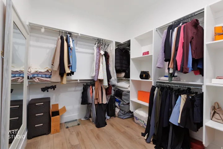 Spacious walk-in closet featuring custom built-in shelving, multiple hanging rods, and wood-finish flooring