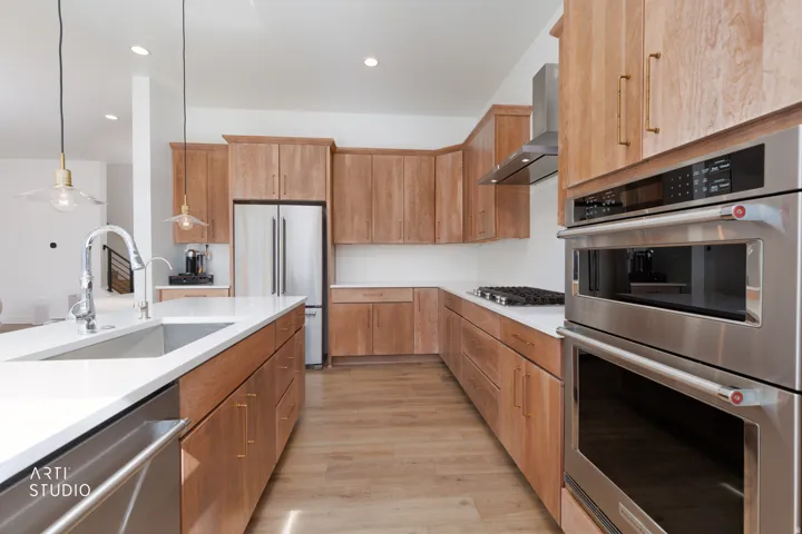 Modern kitchen featuring wood cabinetry, white countertops, stainless steel appliances, and wood-finish flooring