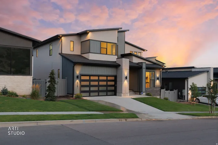 Contemporary architectural design featuring a multi-level roofline, a two-car garage with frosted glass panels, modern exterior lighting, and a concrete driveway