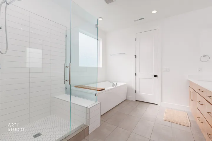 Spacious bathroom featuring a glass-enclosed shower with a built-in bench, a separate soaking tub, and a vanity with natural wood-finish cabinetry