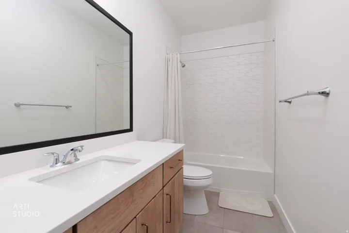 Bathroom with a wood-finish vanity, white countertop, rectangular undermount sink, and a shower-tub combination featuring geometric pattern tile